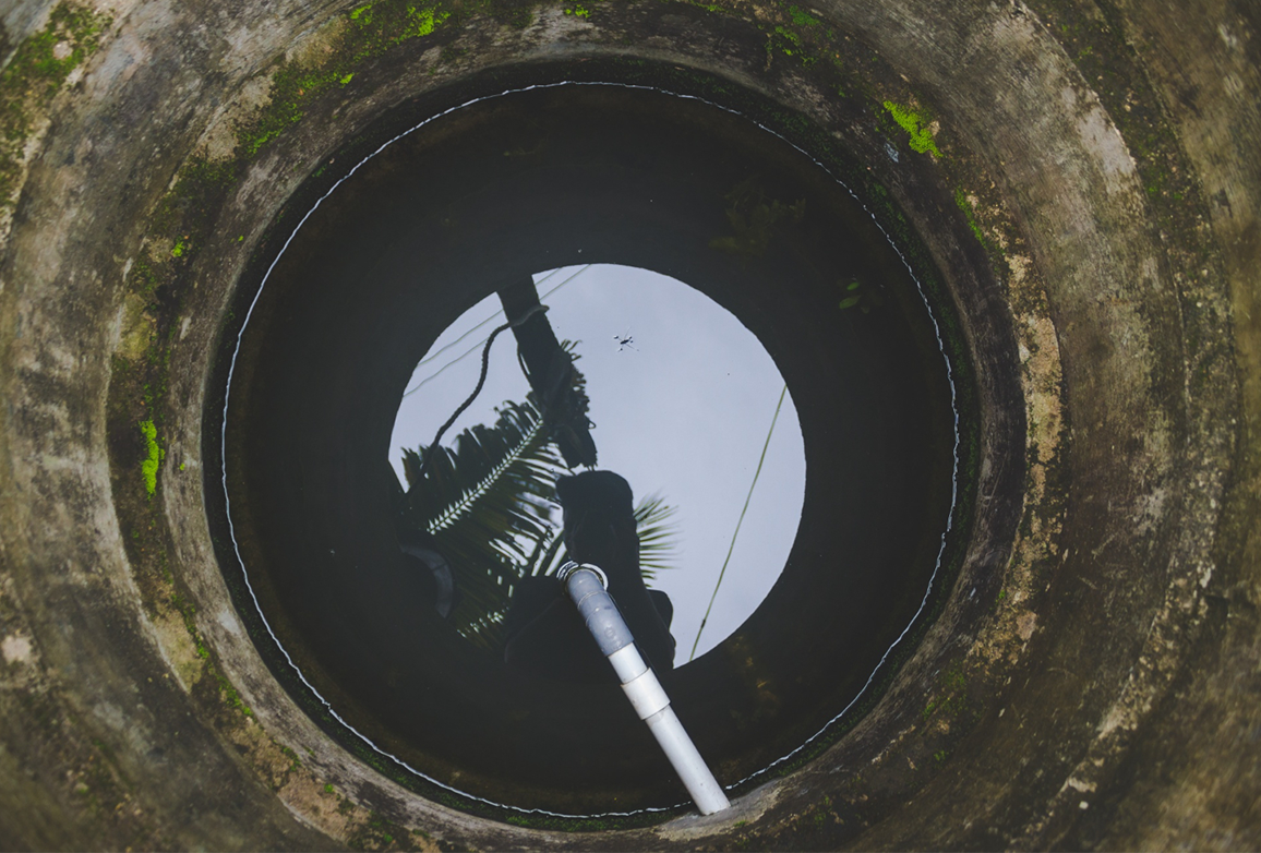 Blick in einen runden Kanalschacht mit Wasser und Pflanzenreflexionen, Kanalreinigung Hannover